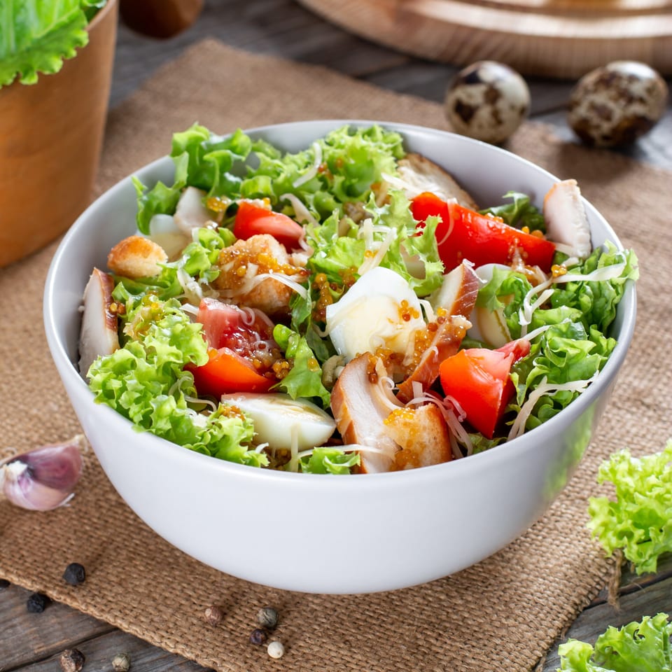 Fresh salad with chicken, lettuce, tomatoes, boiled eggs, and dressing in a white bowl.