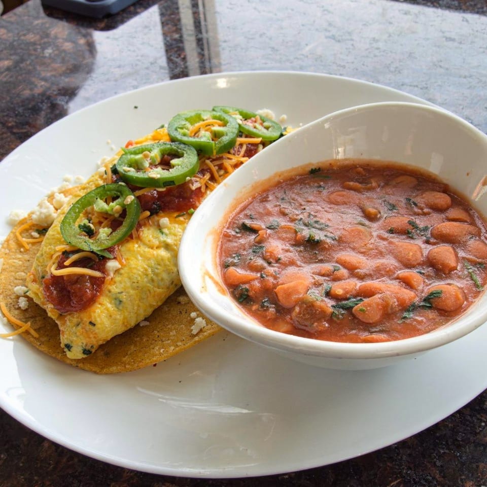 Savory crepe topped with salsa, cheese, and jalapeños, served with a side of beans.