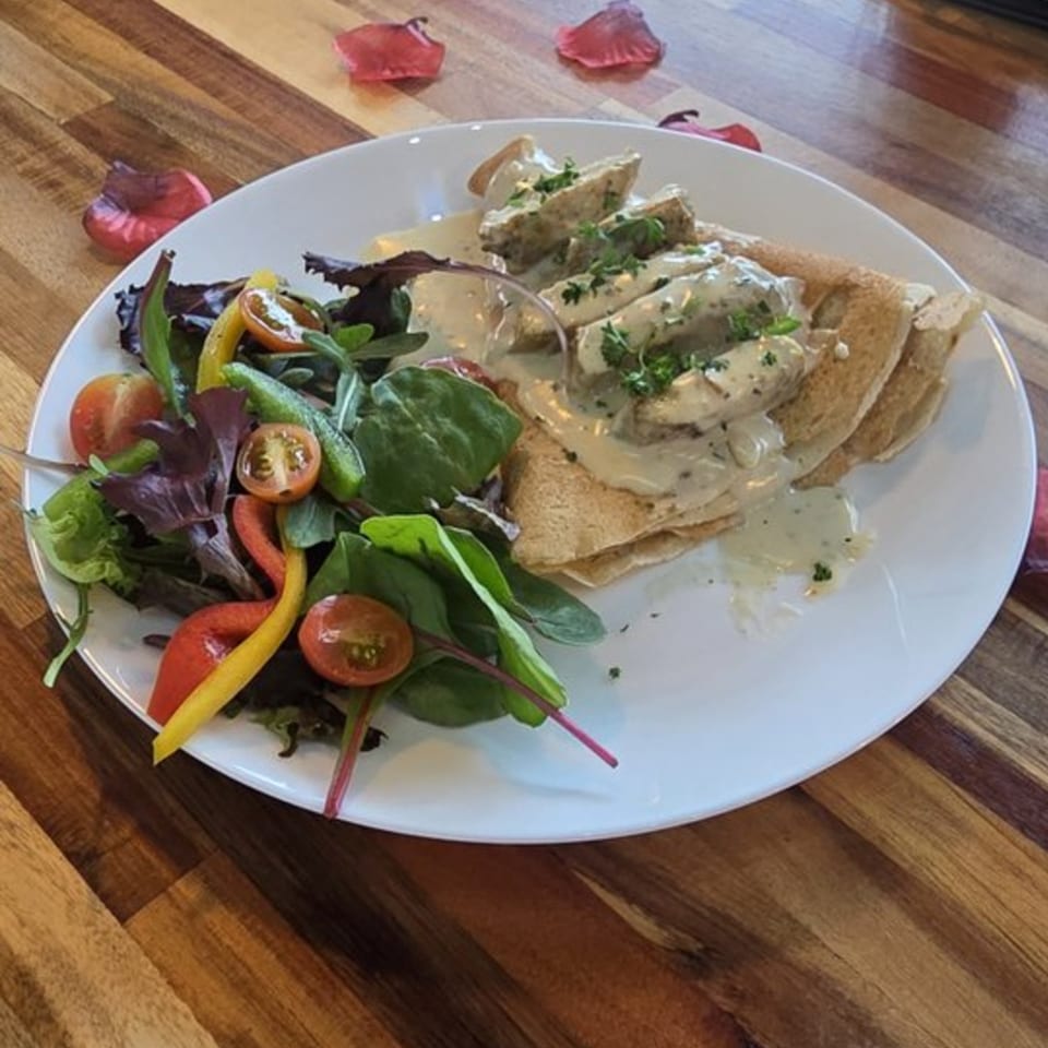 Savory chicken and mushroom crepe with a side salad, garnished with parsley on a white plate.